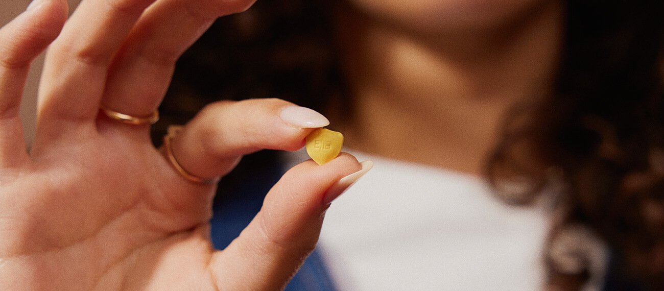Fingers holding a shield shaped pill