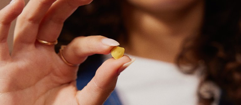 Fingers holding a shield shaped pill